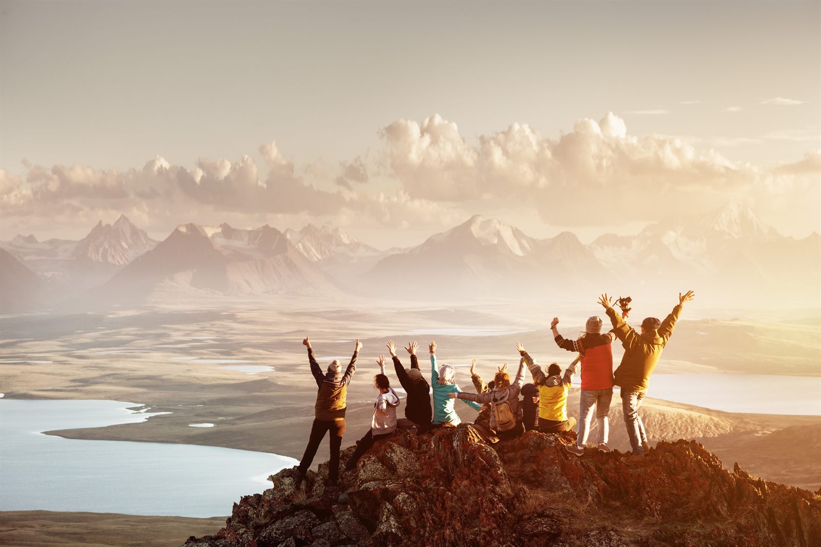 Group of young friends celebrating with arms raised on a hilltop at sunrise