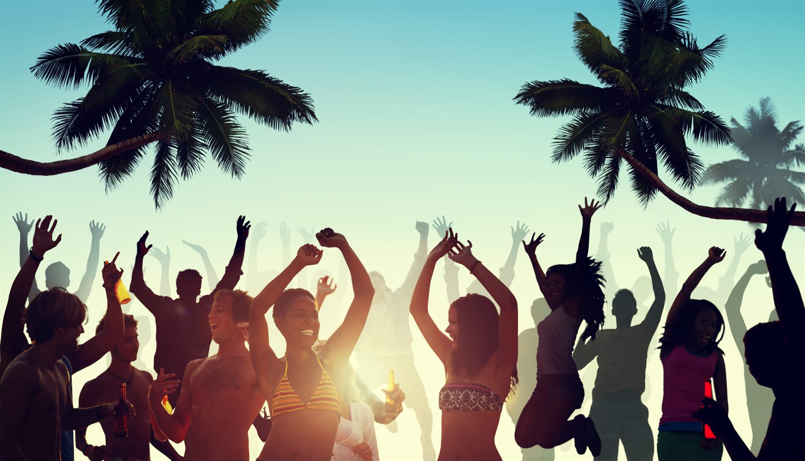 Silhouettes of young people dancing on a beach under palm trees at sunset