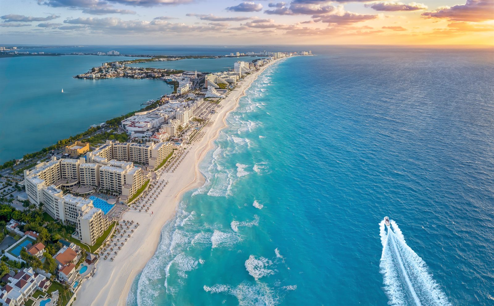 Aerial view of a long white beach and hotel strip beside turquoise water